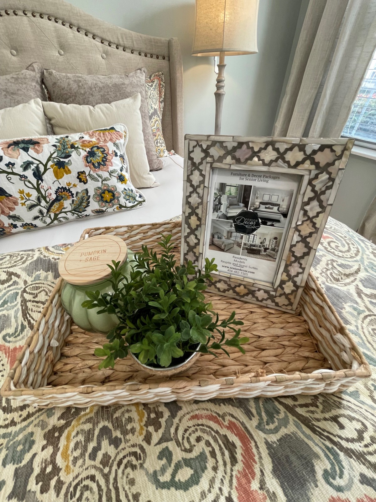 A cozy bedroom setup featuring a decorative tray with a photo frame, a small plant, and a candle on the bed.