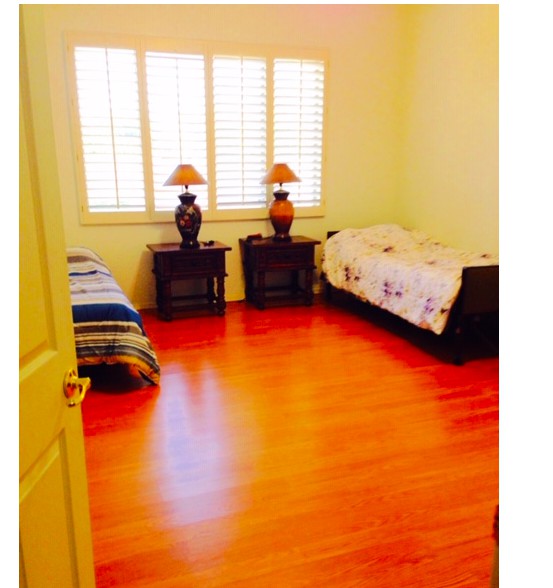 A cozy bedroom with twin beds, wooden flooring, and ample natural light from large windows.