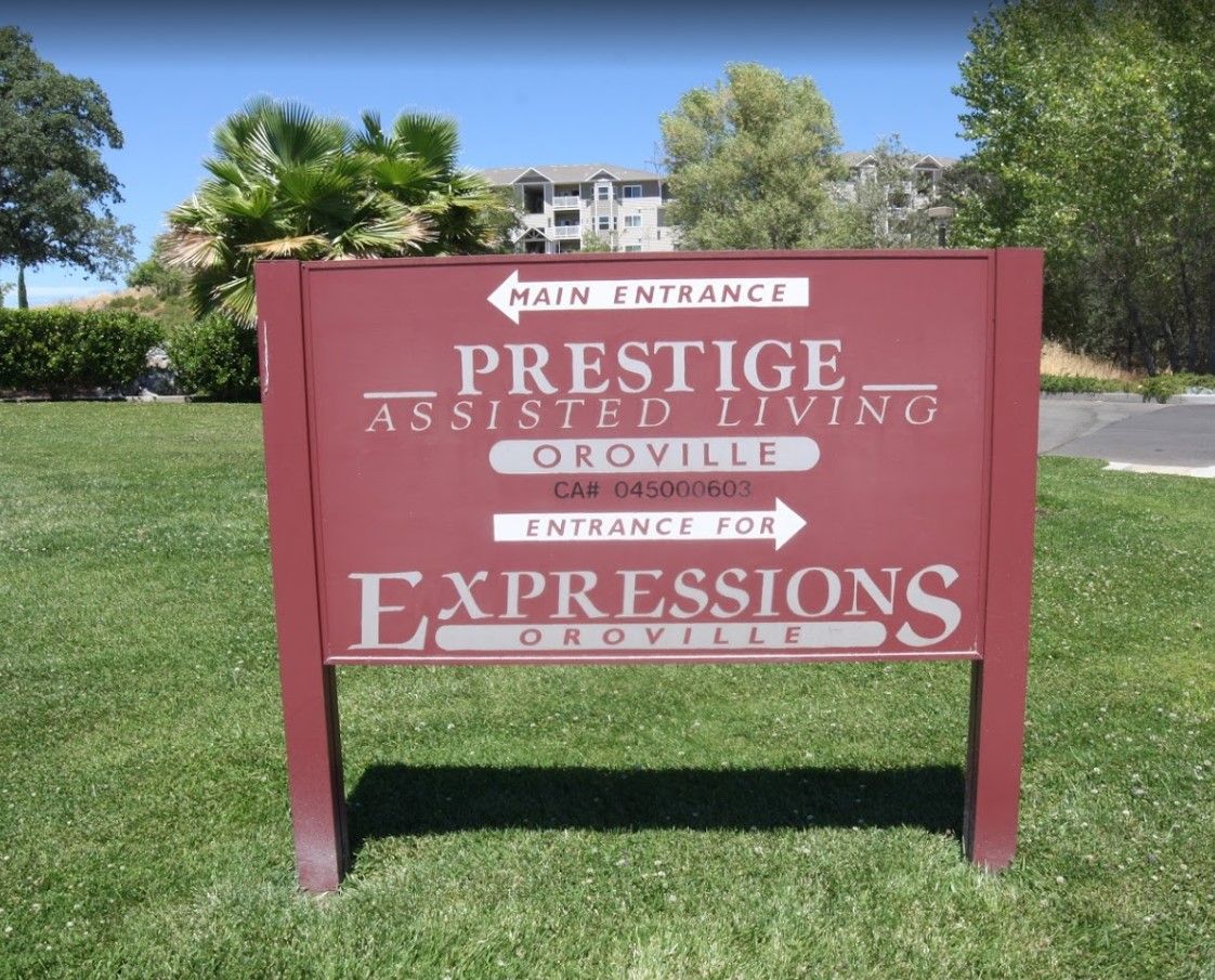 A directional sign for Prestige Assisted Living and Expressions, located on a grassy lawn.