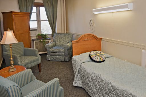 A cozy bedroom setting with a single bed, armchairs, and ambient lighting.