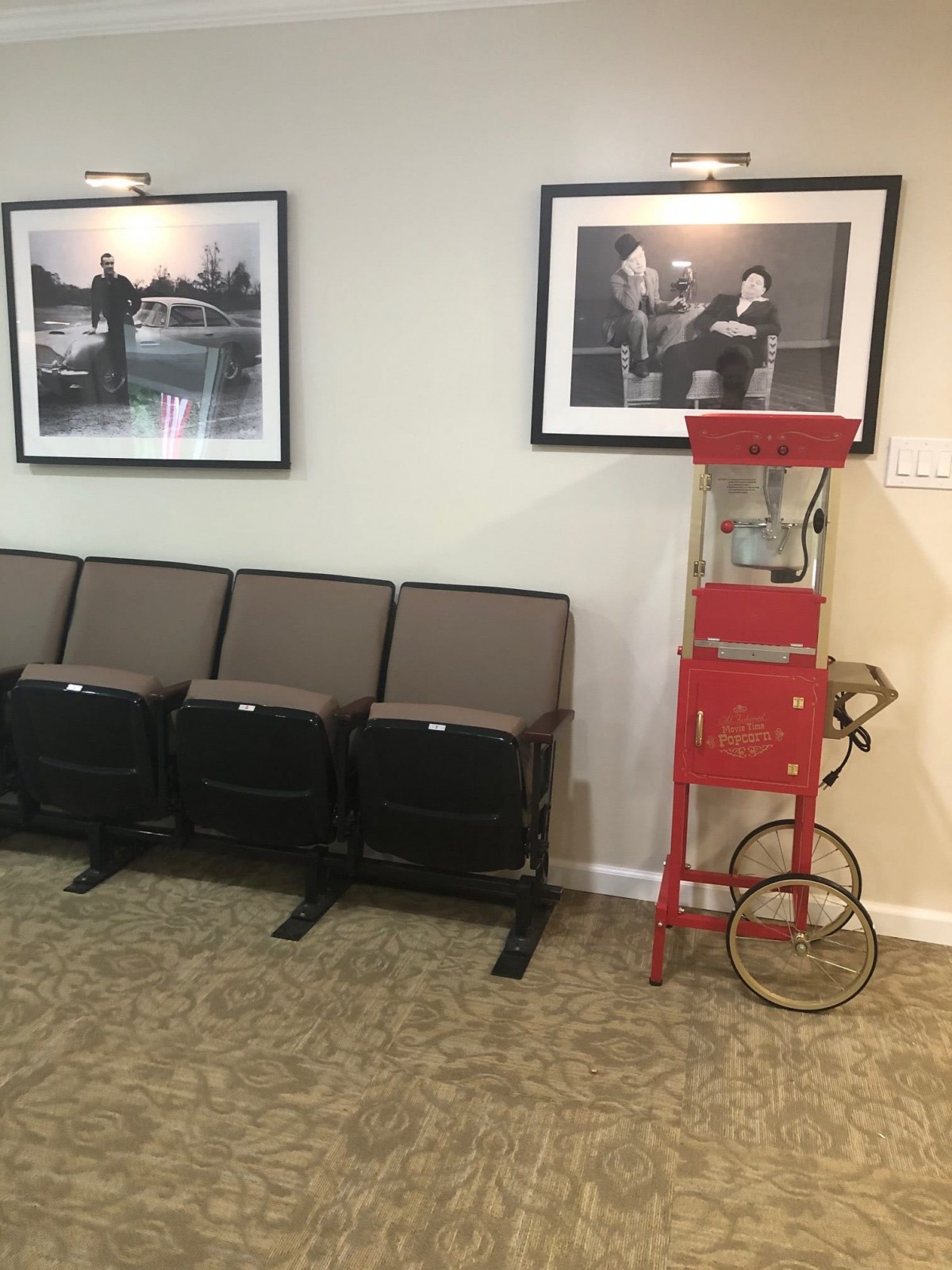 A retro-themed waiting area featuring theater-style seats, a vintage popcorn machine, and framed photographs on the wall.