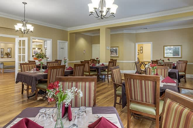 An elegant dining room with neatly arranged tables and chairs, featuring floral centerpieces and a warm ambiance.