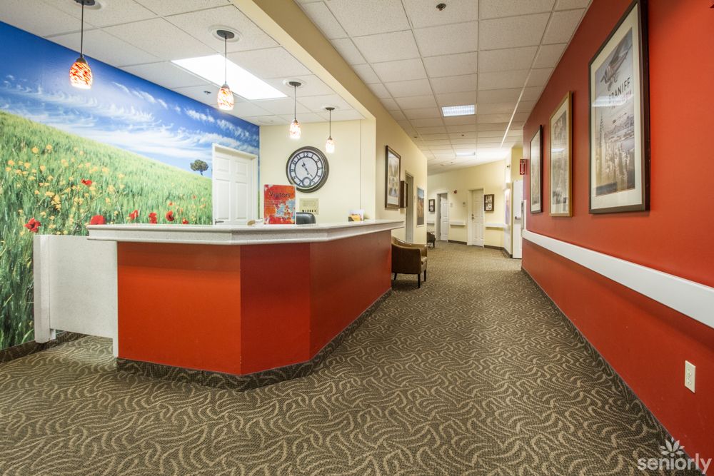 A brightly lit reception area with a red countertop and patterned carpet, leading to an office hallway.