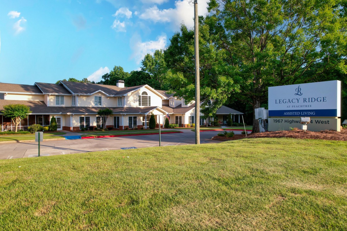 A large residential building with a sign, surrounded by trees and grass under a blue sky.
