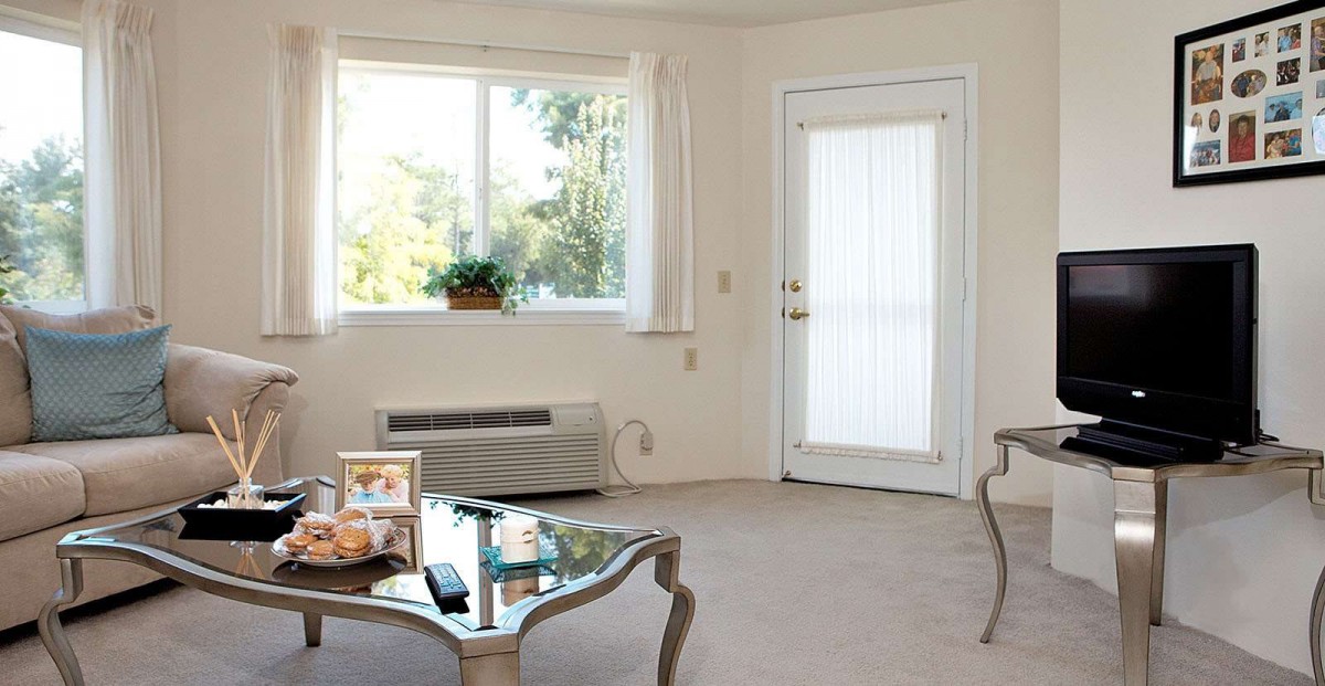 A cozy living room with a window and door, featuring a glass coffee table and decorative items.