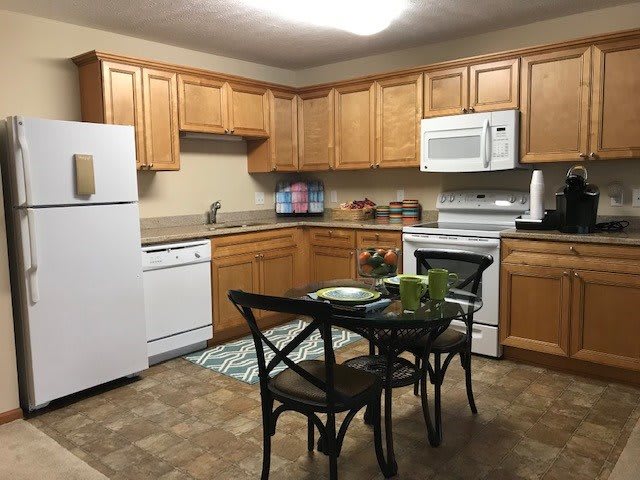 A cozy kitchen with wooden cabinets, featuring modern appliances and a small dining table.
