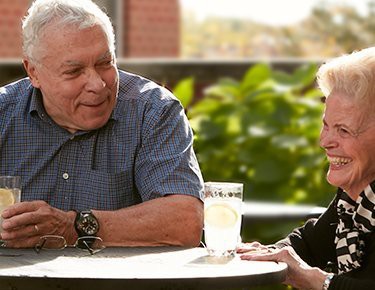 Two elderly people enjoying a conversation outdoors on a sunny day.