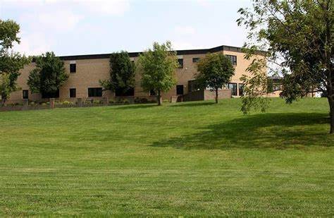 A view of a building with a large grassy lawn and several trees under a clear sky.