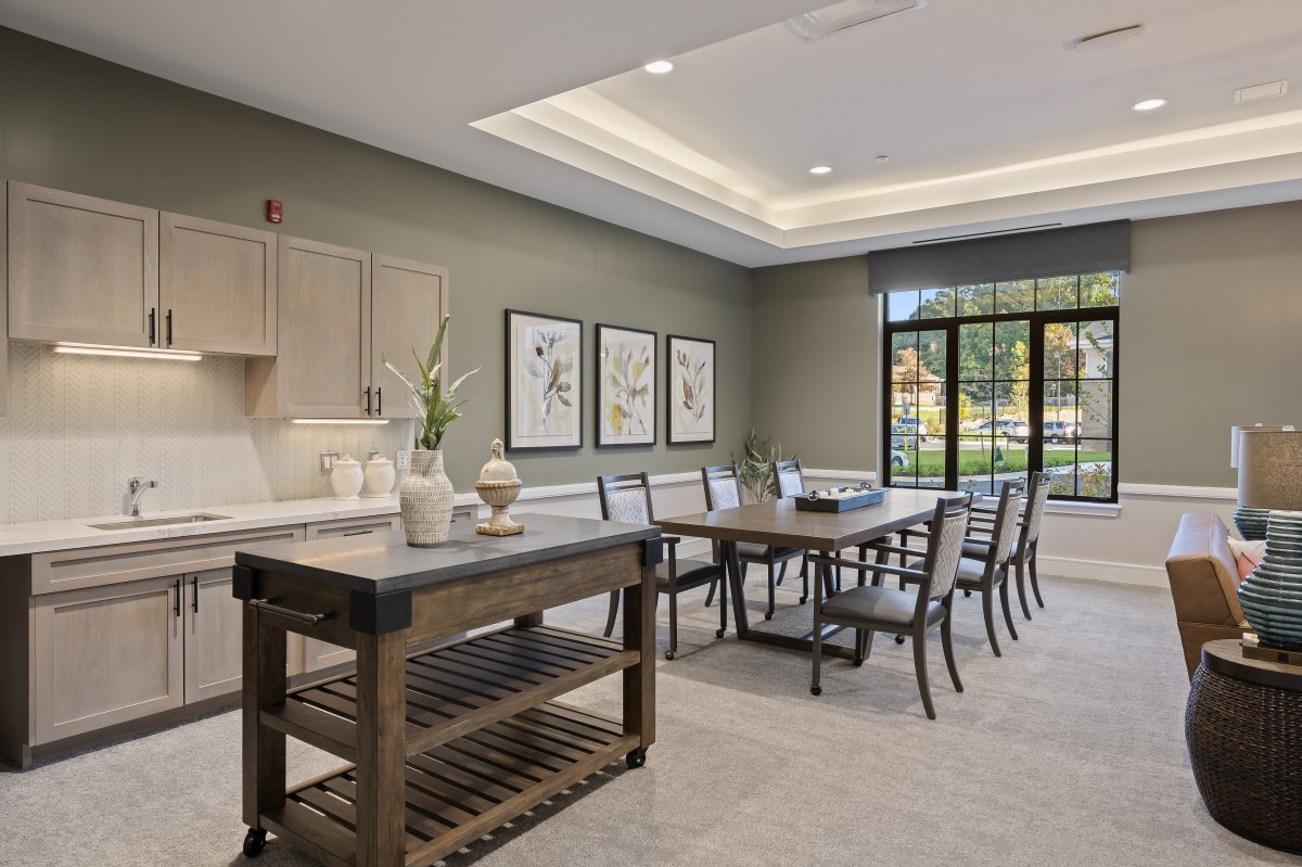 A modern dining room with a large table, chairs, and a kitchen island, accented by wall art and ample natural light.