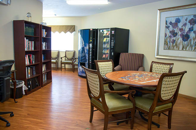A cozy reading and relaxation area featuring a table with chairs, bookshelves, and vending machines.