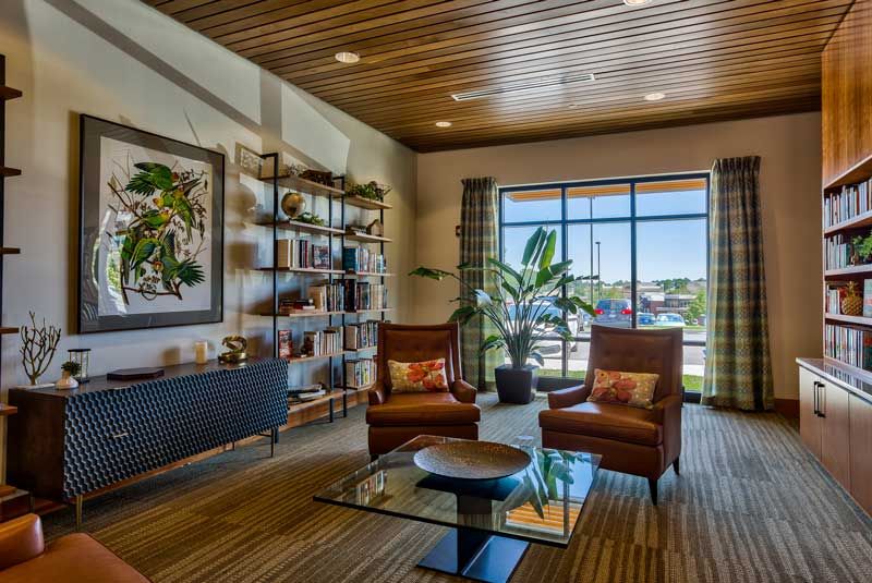 A modern living room with leather chairs, a glass coffee table, and a bookshelf, featuring large windows and decorative plants.