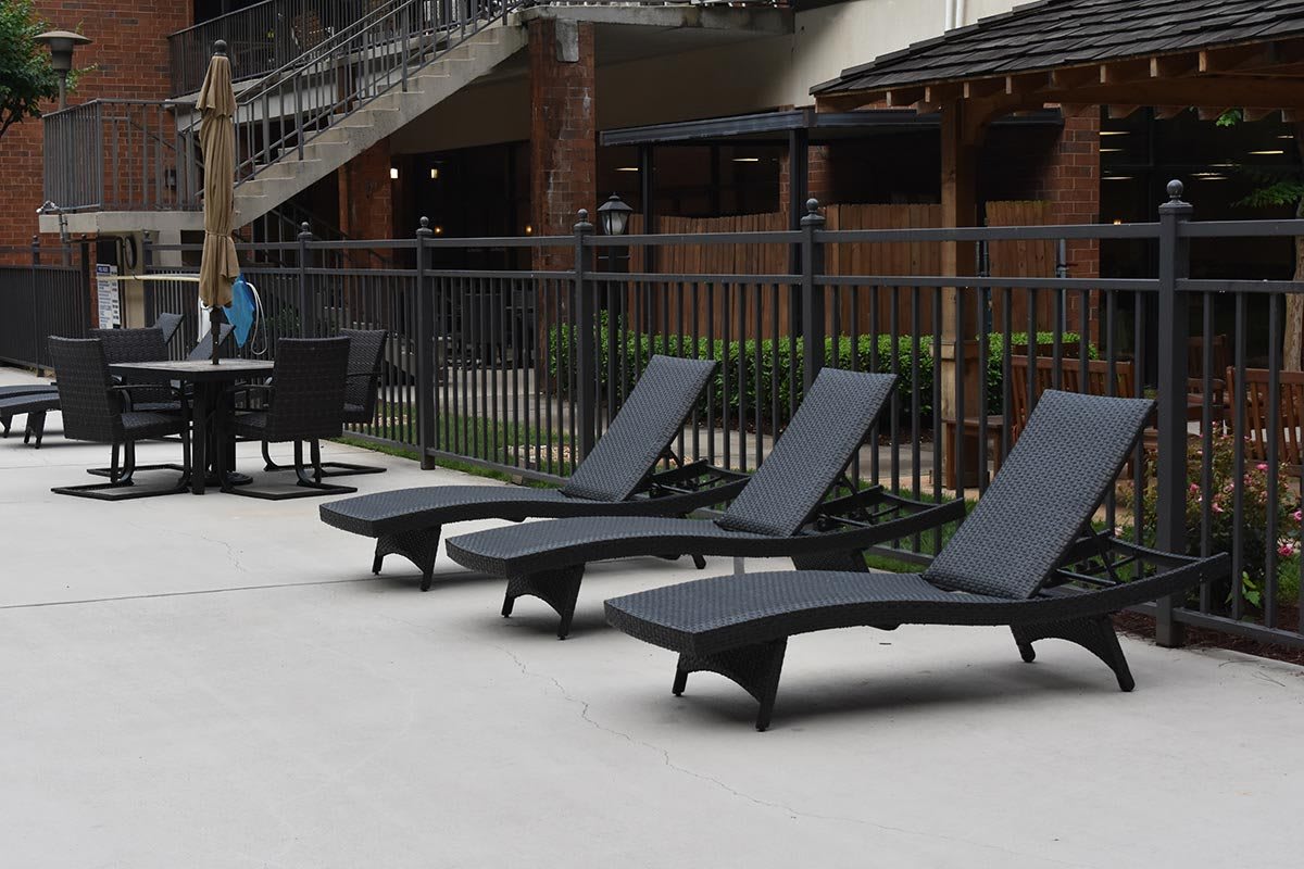 A row of black lounge chairs by a poolside patio with a nearby table and chairs.