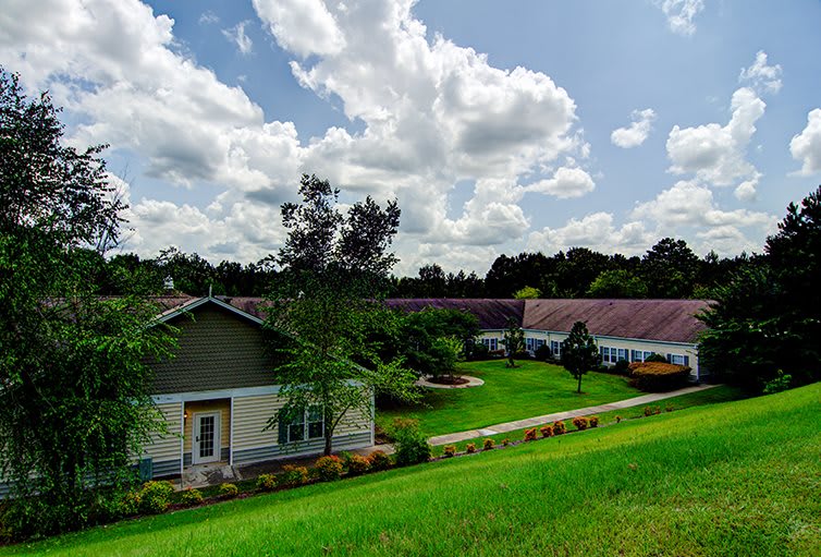 A picturesque countryside scene with a house surrounded by lush greenery and a cloudy sky.