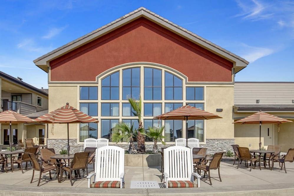 A building with large windows and outdoor seating featuring chairs, tables, and umbrellas.