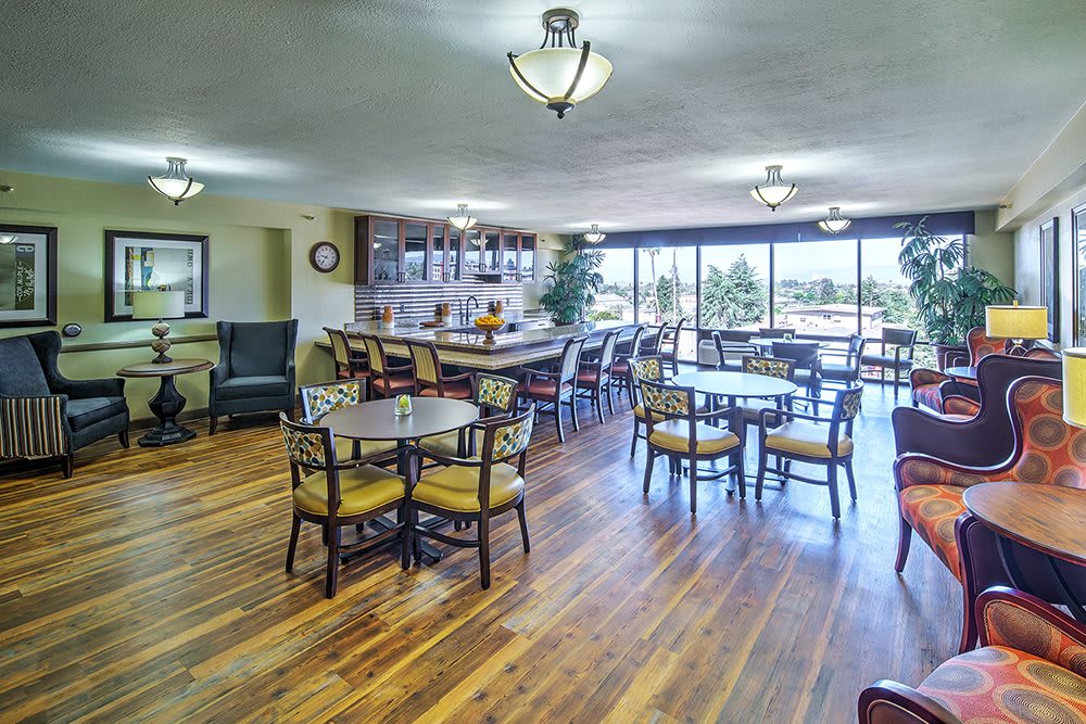 A spacious dining area with wooden floors, tables, and chairs, featuring a bar and large windows.