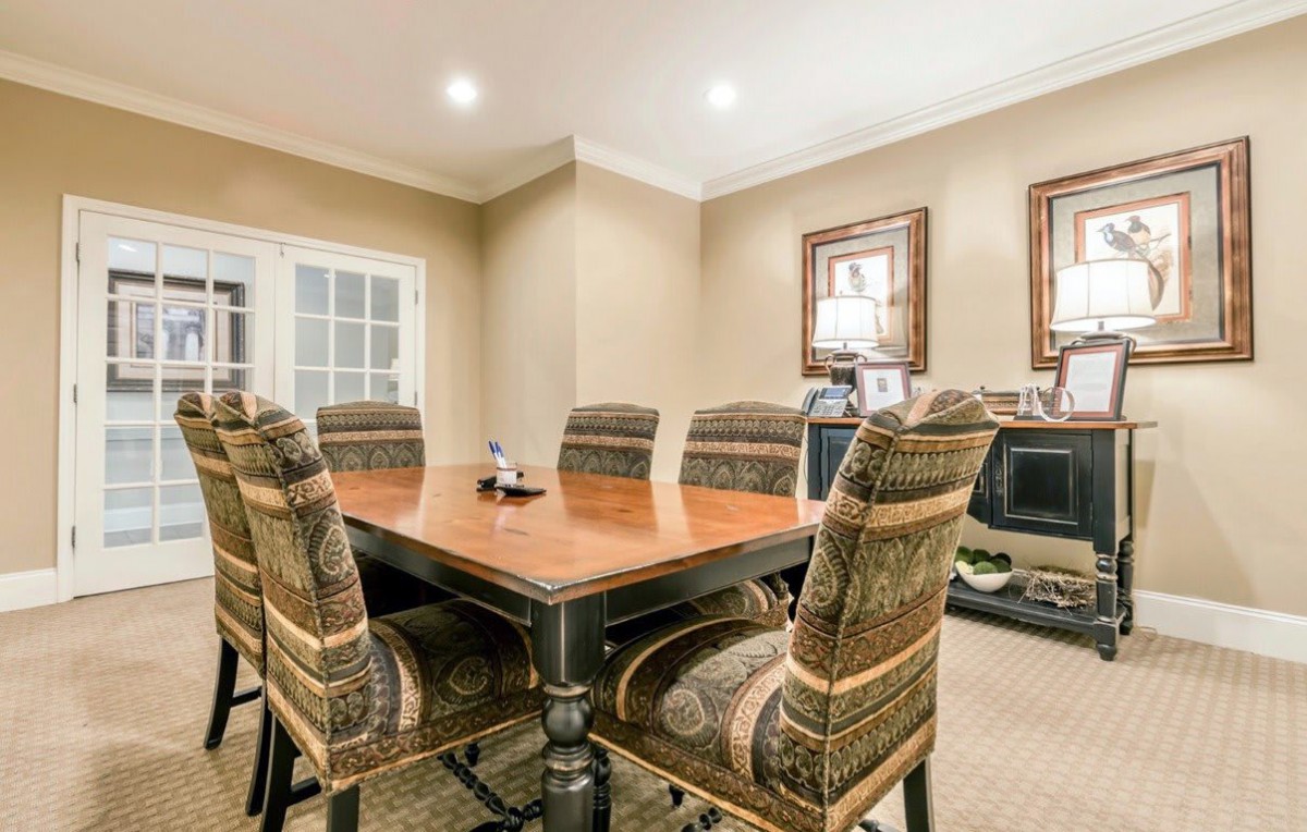 A well-appointed dining room with a large wooden table surrounded by upholstered chairs, featuring warm lighting and decorative artwork.