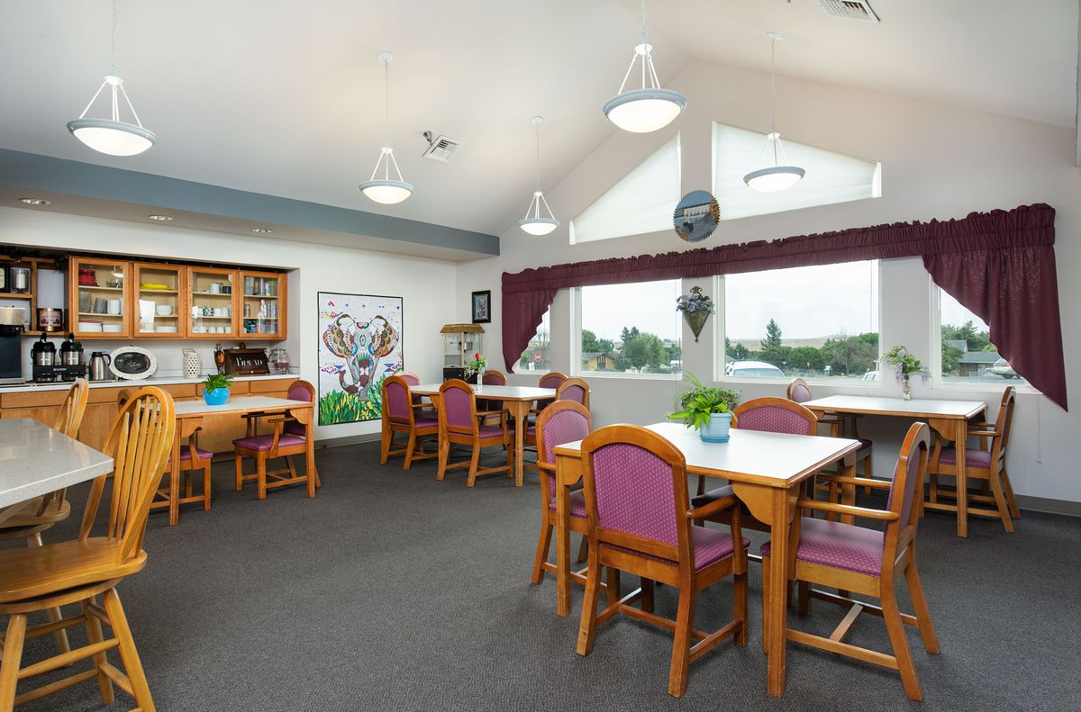 A spacious dining room with multiple tables and chairs, featuring large windows and decorative elements.