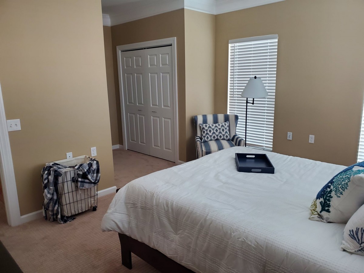 A neatly arranged bedroom with a bed, chair, and lamp.