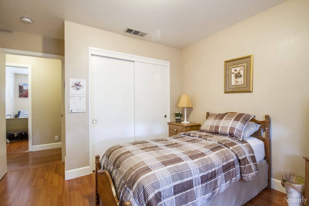 A cozy bedroom with a neatly made bed, a bedside lamp, and a sliding closet door on hardwood flooring.