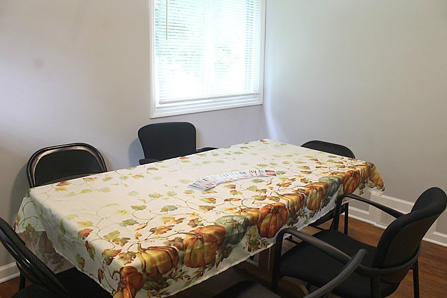 A small room with a table covered in a patterned tablecloth and surrounded by chairs.
