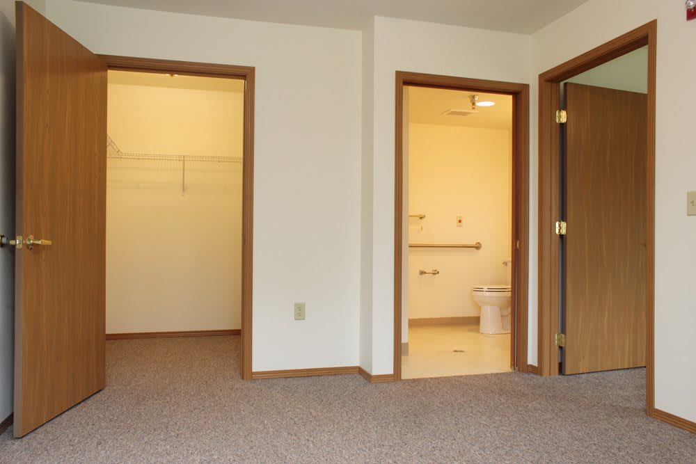 An empty room with a carpeted floor, featuring doorways leading to a closet and a bathroom.