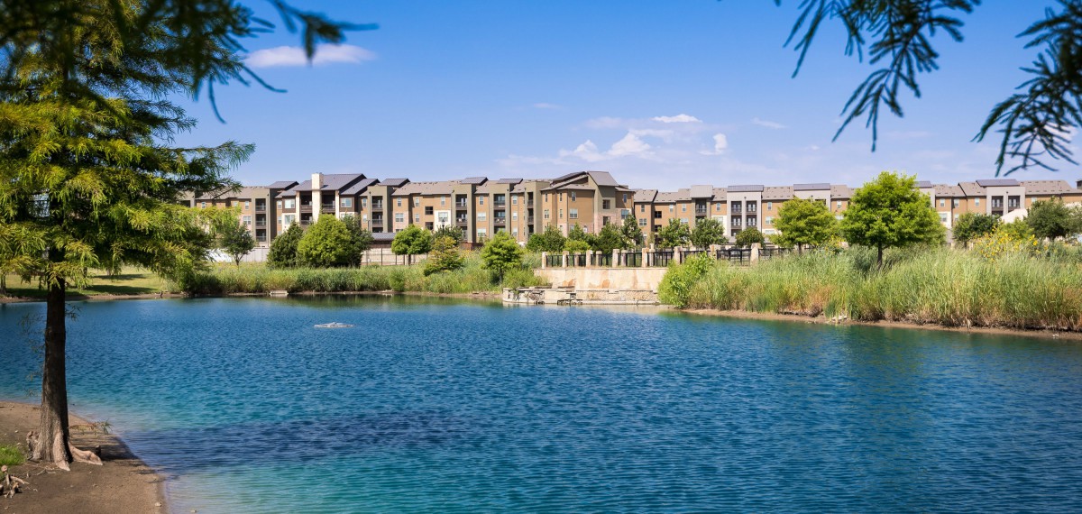 A scenic view of residential buildings by a tranquil lake surrounded by greenery.