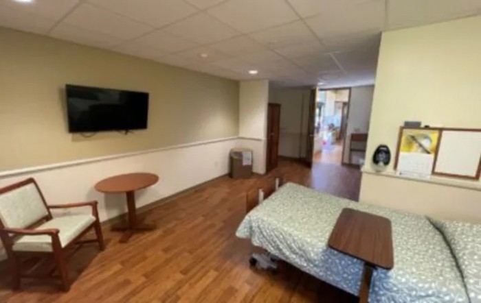 A hospital room featuring a bed, television, table, and chair.