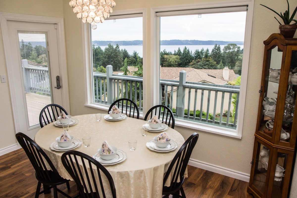 A dining room with a table set for six, overlooking a scenic view through large windows.