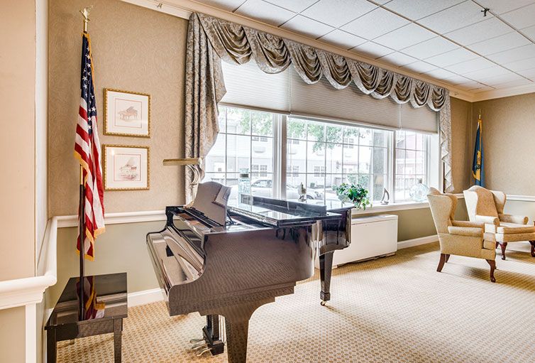 A cozy room featuring a grand piano and large windows with elegant drapes, accompanied by an American flag.