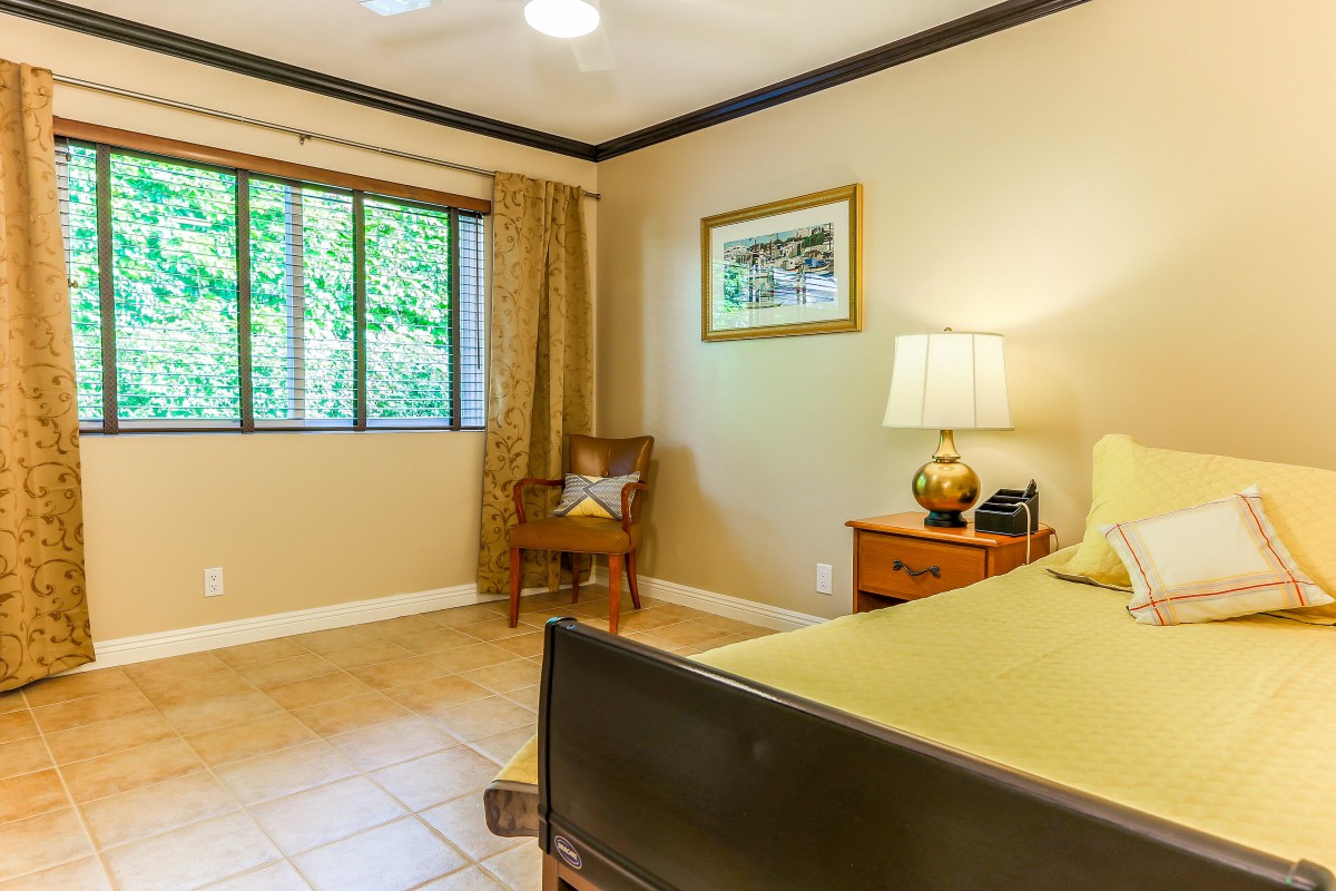 A cozy bedroom featuring a bed, chair, and bedside table with a lamp.