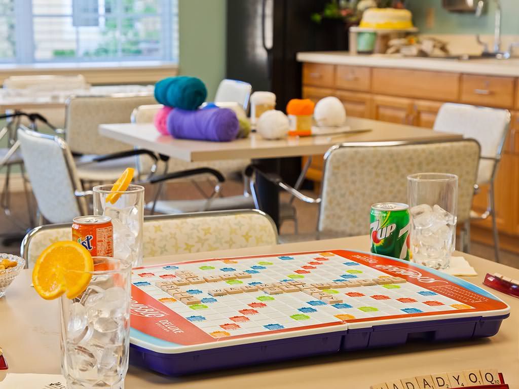 A cozy kitchen setting featuring a colorful board game on the table, with yarn and beverages in the background.