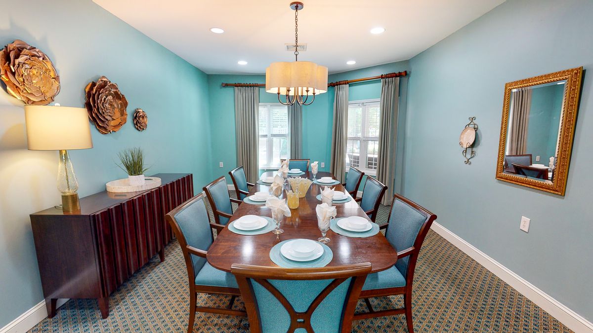A stylish dining room with turquoise walls, featuring a long wooden dining table set for a meal, surrounded by matching chairs and illuminated by a chandelier.