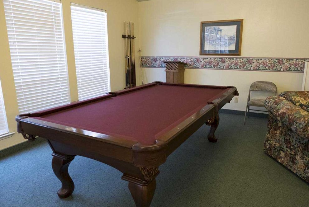 A billiards table with a maroon felt surface in a well-lit game room.