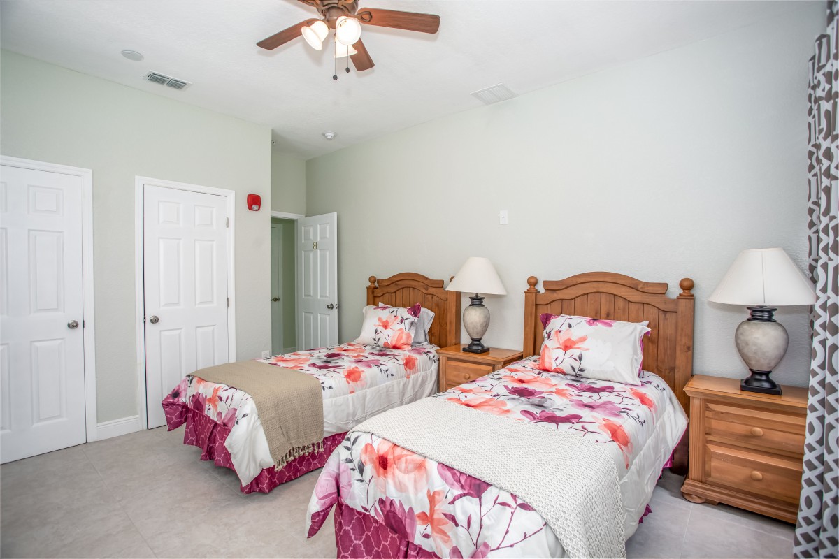 A cozy bedroom with two twin beds featuring floral bedding and a wooden nightstand adorned with a lamp, all under a ceiling fan.