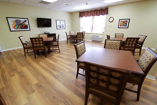 A dining room with multiple tables and chairs, featuring a television on the wall and a window providing natural light.