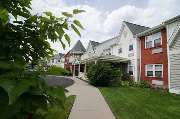 A picturesque residential building with a well-maintained landscape and a clear sidewalk, set against a cloudy sky.