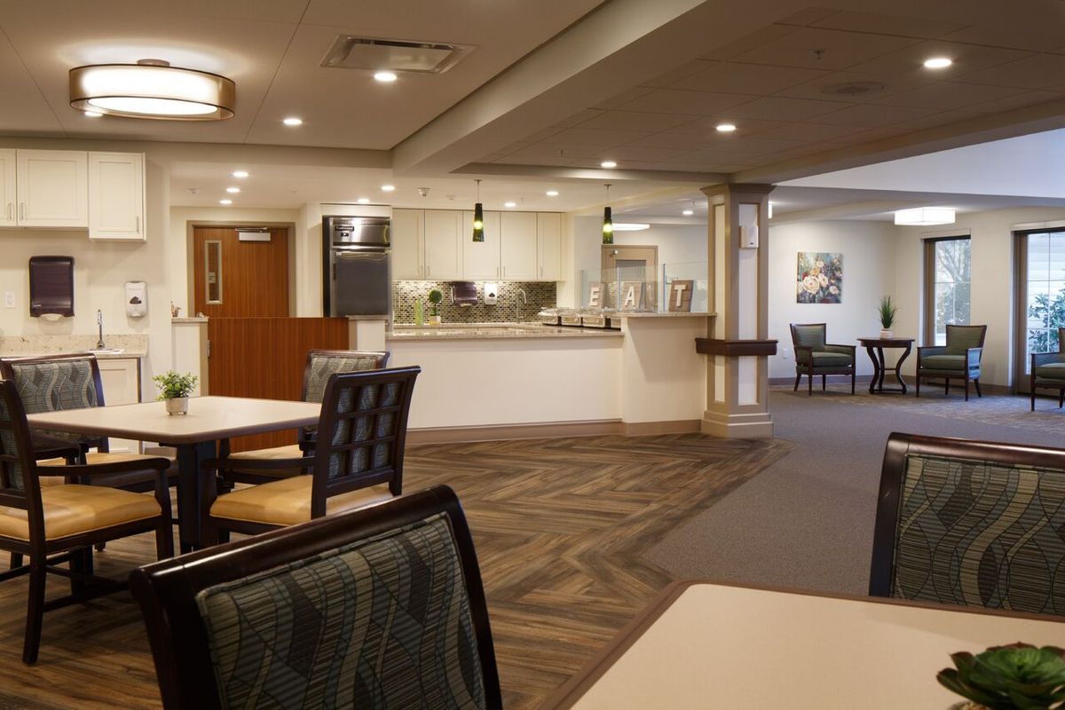 A modern dining area with a view of the kitchen, featuring neatly arranged tables and chairs.