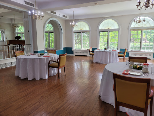 A spacious and elegantly decorated event space featuring round tables, colorful chairs, and ample natural light.