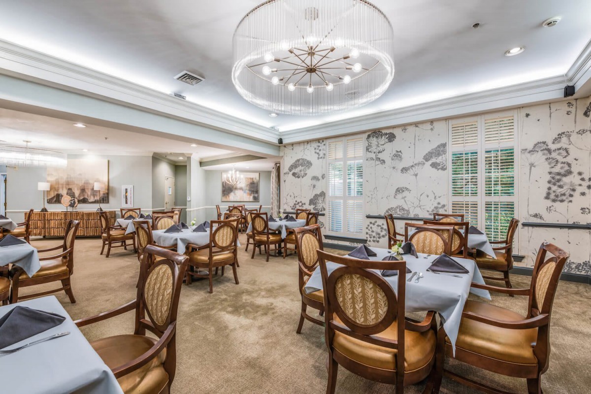 An elegant dining area with neatly arranged tables and chairs under a chandelier.
