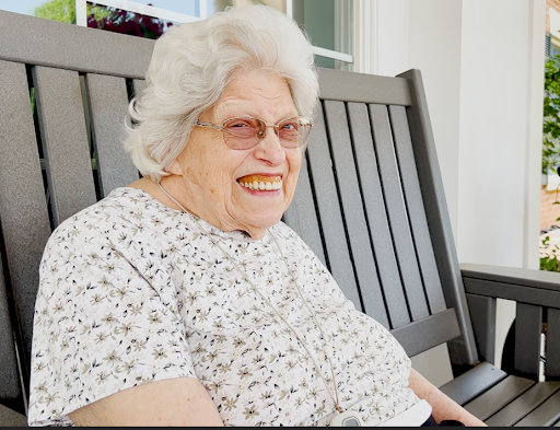 A joyful elderly woman enjoying a sunny day on her porch.