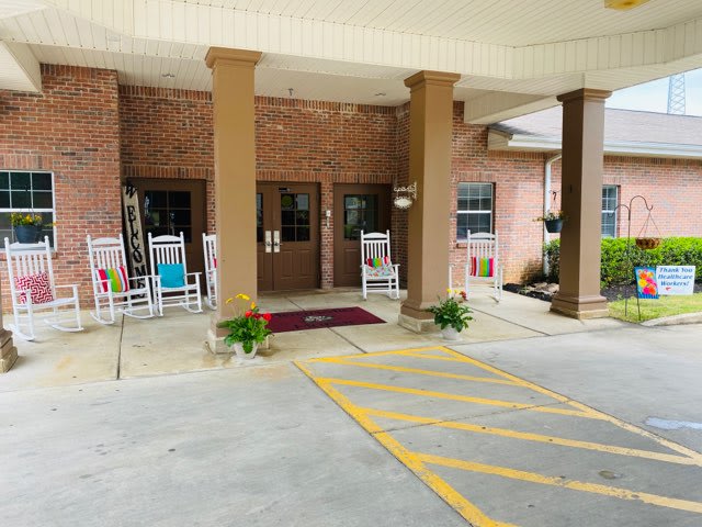 Entrance of a building with rocking chairs and plants under a covered walkway.