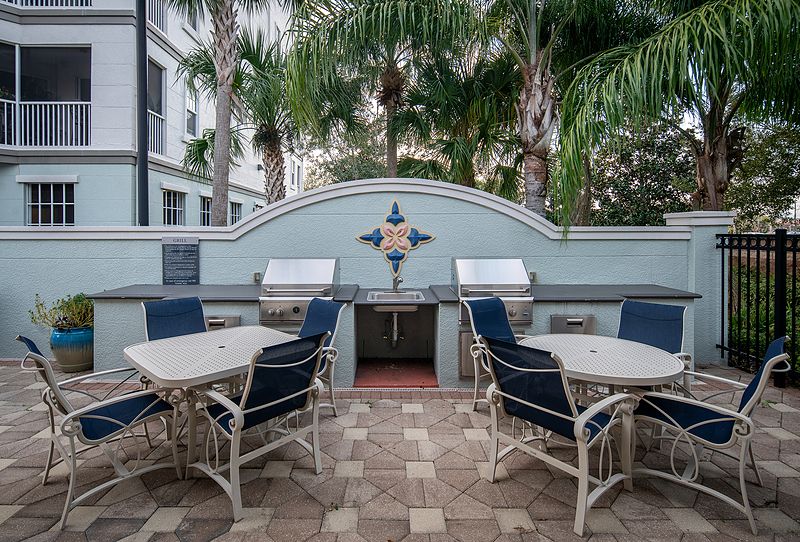 Outdoor patio with grill and seating area surrounded by palm trees.