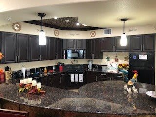 A modern kitchen with dark cabinets and granite countertops, featuring pendant lighting and decorative elements.