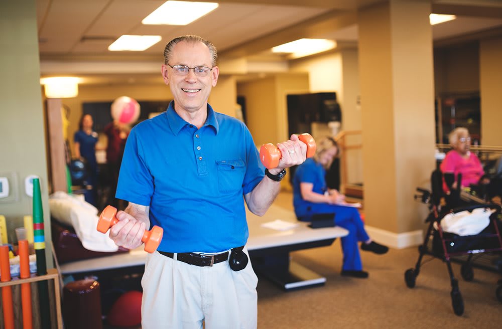 An elderly man exercising with dumbbells in a gym setting.