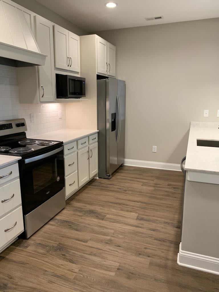 A modern kitchen with white cabinets, stainless steel appliances, and wood flooring.