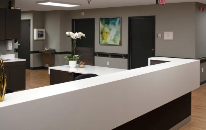 A modern reception area with a white desk, decorative flowers, and abstract artwork on the wall.
