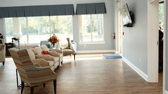 A cozy living room with natural light, featuring comfortable seating and a wall-mounted TV.