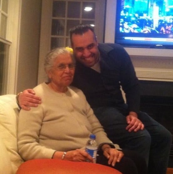 Two people sitting together in a living room with a TV on in the background.