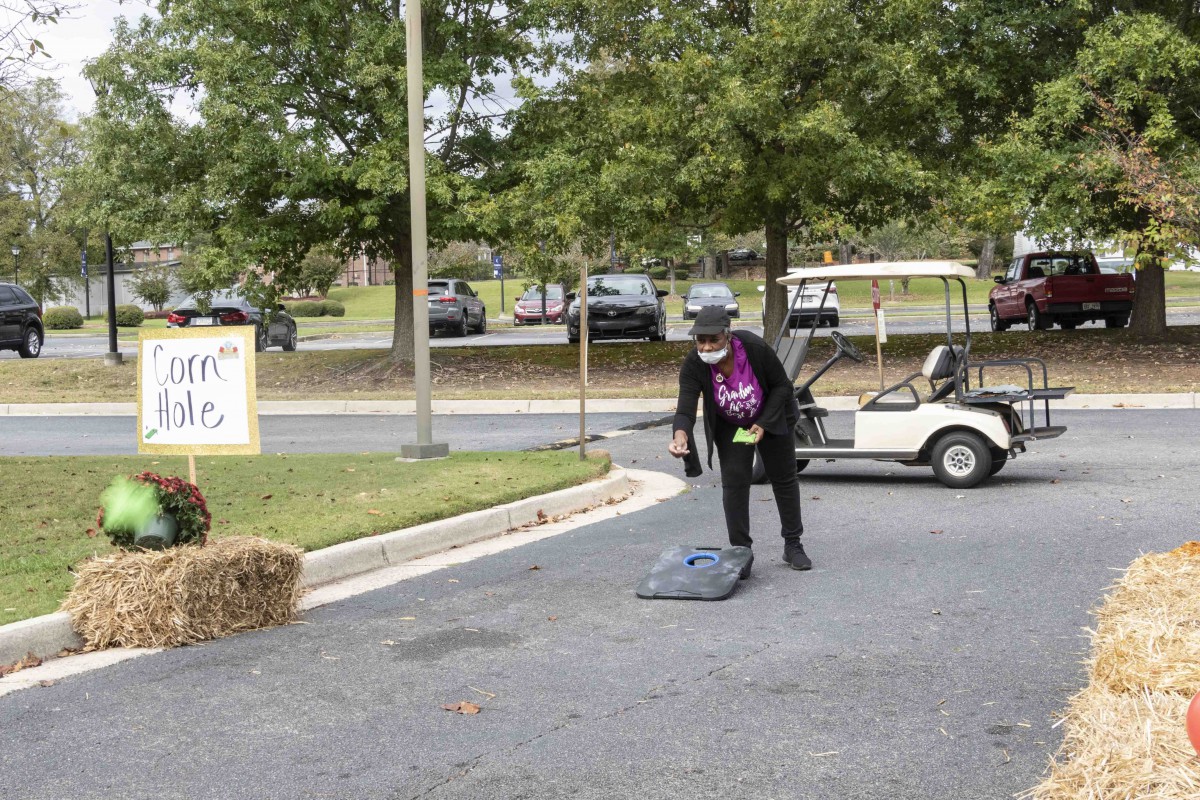 A person in a Halloween costume stands on the street near a golf cart, surrounded by autumn decorations.
