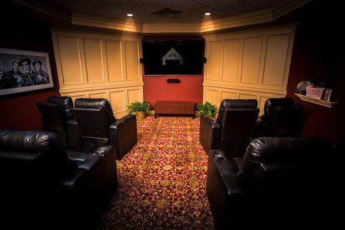 A cozy home theater with leather seating and a screen, featuring dim lighting and a patterned carpet.